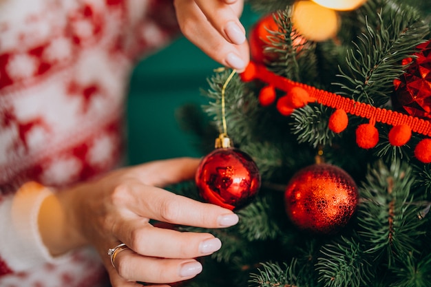 Mãos femininas fechem, decorando a árvore de Natal com bolas vermelhas