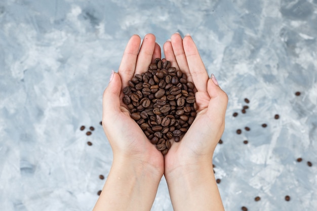 Mãos femininas segurando grãos de café estendidas sobre um fundo cinza sujo