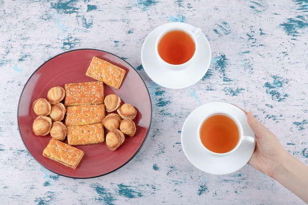 Mãos femininas segurando uma xícara de chá com nozes de shortbread com leite condensado.