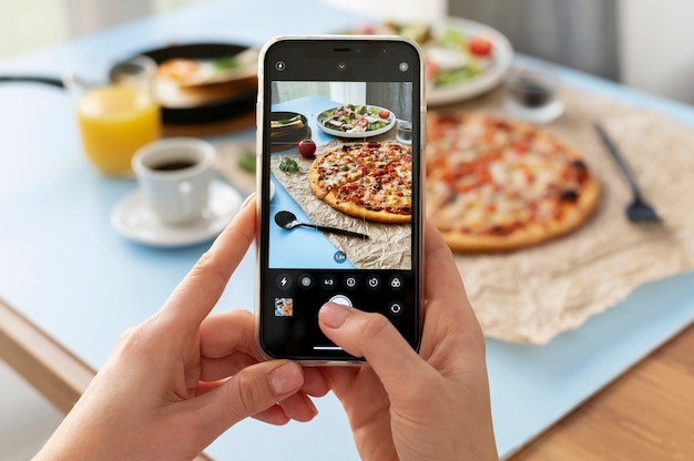 Mãos femininas tirando foto de pizza fatiada e prato de salada