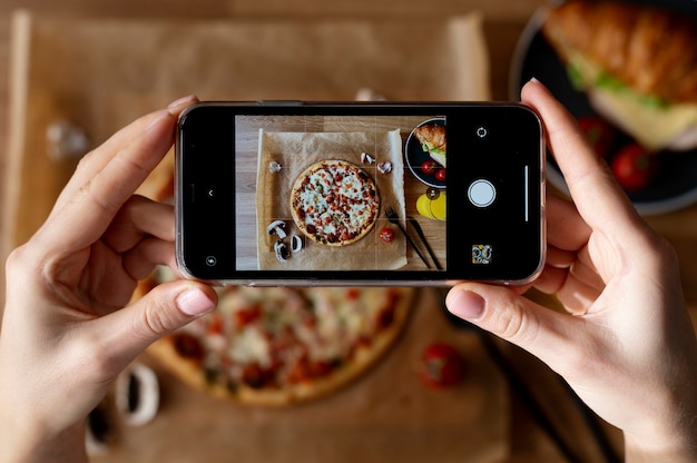 Mãos femininas tirando foto de pizza fatiada