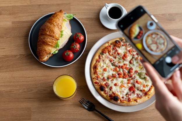 Mãos femininas tirando foto de uma pizza fatiada e um croissant com queijo