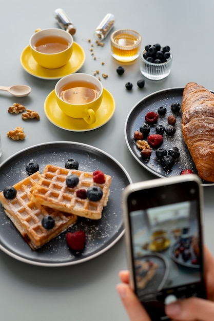 Foto grátis mãos femininas tirando foto de waffles com frutas e duas xícaras de chá