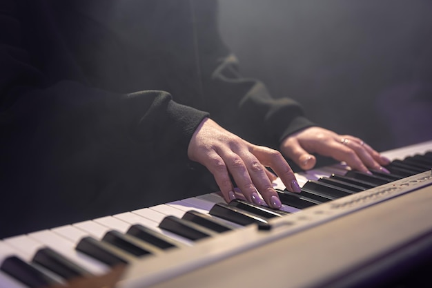 Mãos femininas tocando teclas de piano em uma sala escura e enevoada