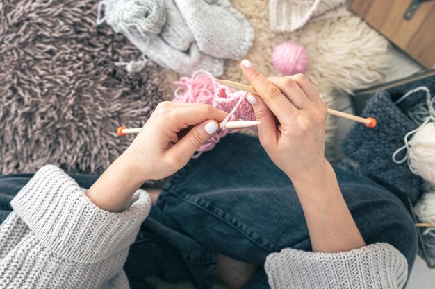 Mãos femininas tricotam lenço rosa quente em casa vista superior