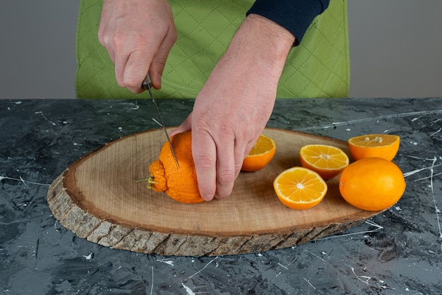 Mãos masculinas cortando limão fresco na mesa de mármore.