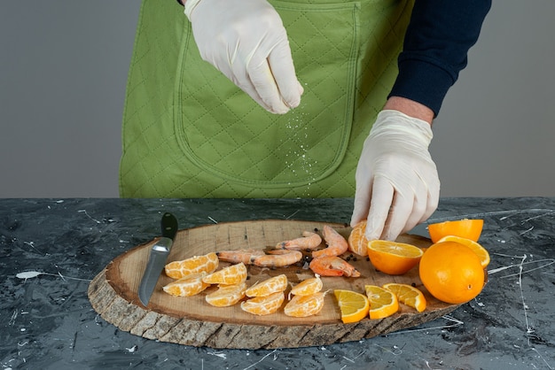 Mãos masculinas, cortando os camarões e as frutas na mesa de mármore.