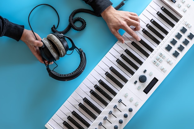 Mãos masculinas tocando teclas musicais e segurando fones de ouvido no fundo azul, plano leigo, conceito de criatividade musical.