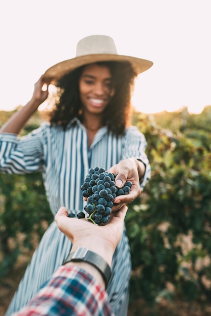 Mãos que compartilham um cacho de uvas com uma mulher feliz e turva