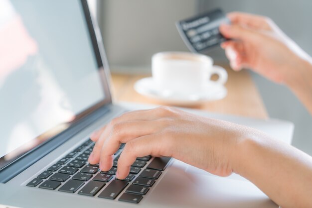 Mãos que prendem um cartão de crédito e usam o computador portátil para o on-line