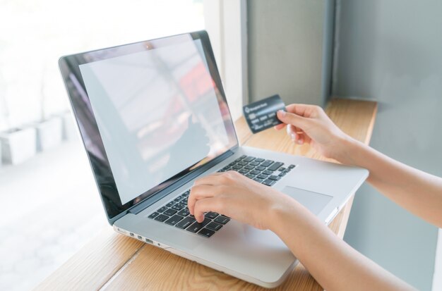 Mãos que prendem um cartão de crédito e usam o computador portátil para o on-line