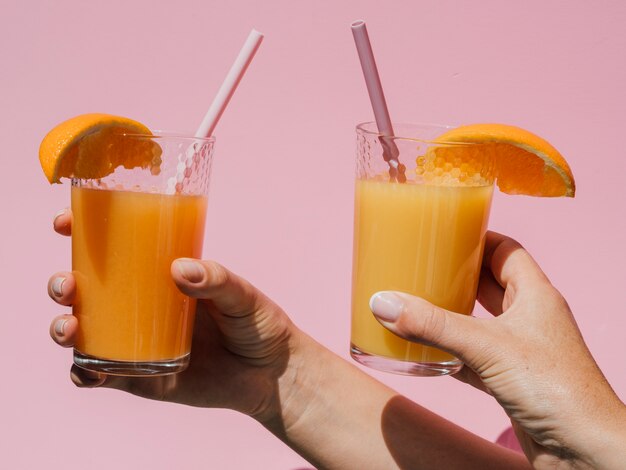 Mãos segurando copos com vista frontal de suco de laranja natural