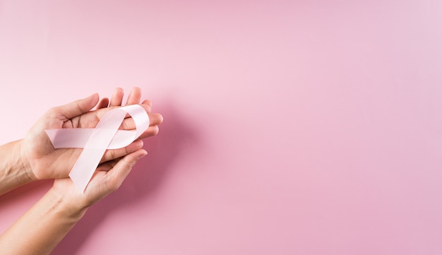 Mãos segurando fitas cor de rosa para a conscientização do câncer de mama.