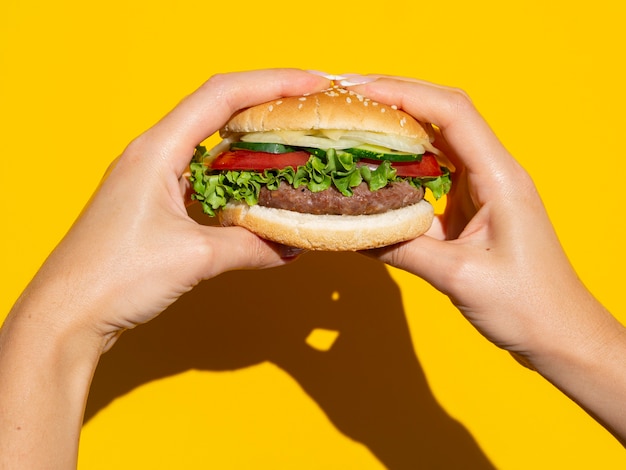 Mãos segurando hambúrguer perfeito em fundo amarelo