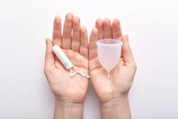 Mãos segurando itens de higiene produzidos para as mulheres durante o período menstrual, com copo e tampão menstruais