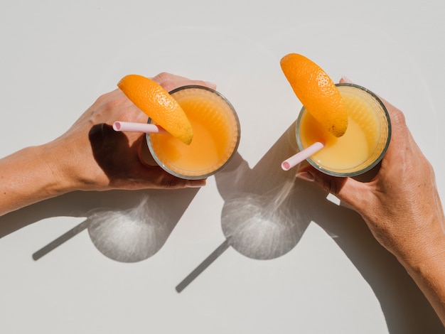 Foto grátis mãos segurando óculos com vista superior de suco de laranja natural