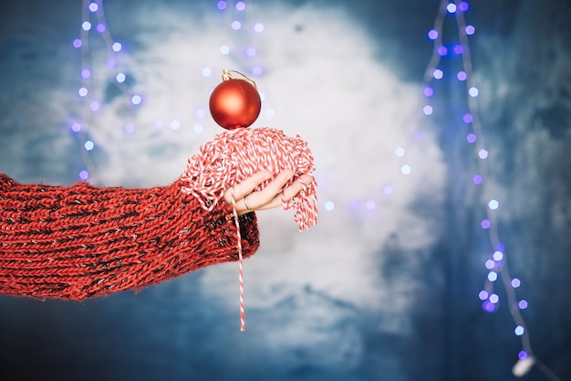 Mãos segurando pequena bola vermelha de natal