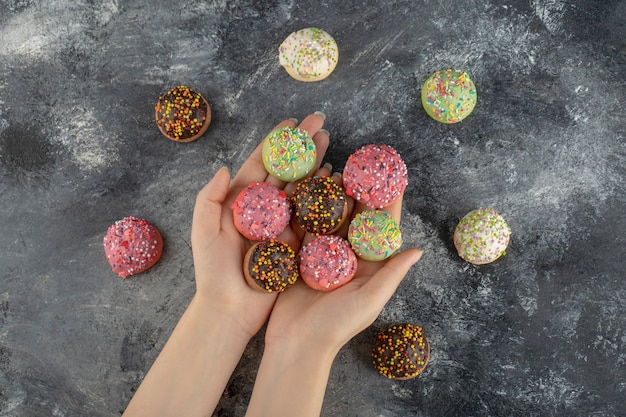 Mãos segurando rosquinhas pequenas doces coloridas com granulado.