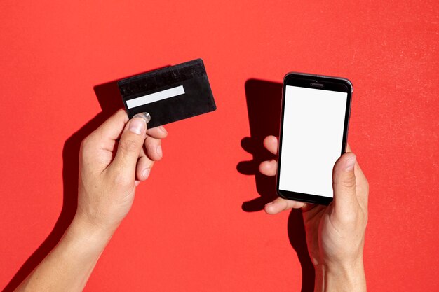 Mãos segurando um cartão de crédito e um telefone simulado