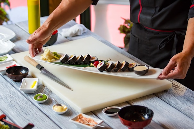 Mãos segurando um prato com sushi. rolos de sushi com especiarias. rolinhos futomaki preparados pelo chef. prato mais saboroso em restaurante japonês.