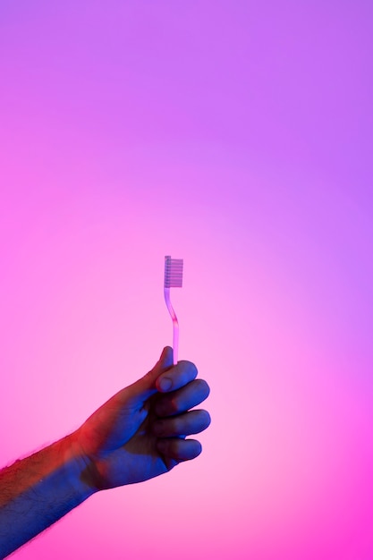 Mãos segurando uma escova de dentes sobre fundo gradiente