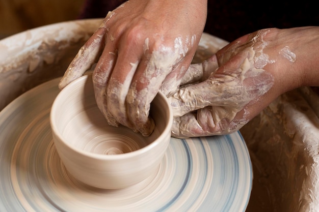 Mãos sujas modelando em argila em uma roda de oleiro
