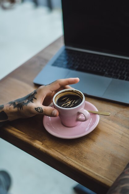 mãos tatuadas, café e laptop