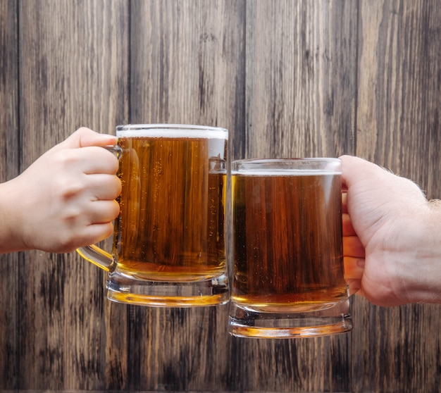 Foto grátis mãos tinindo canecas de cerveja na vista lateral de madeira rústica