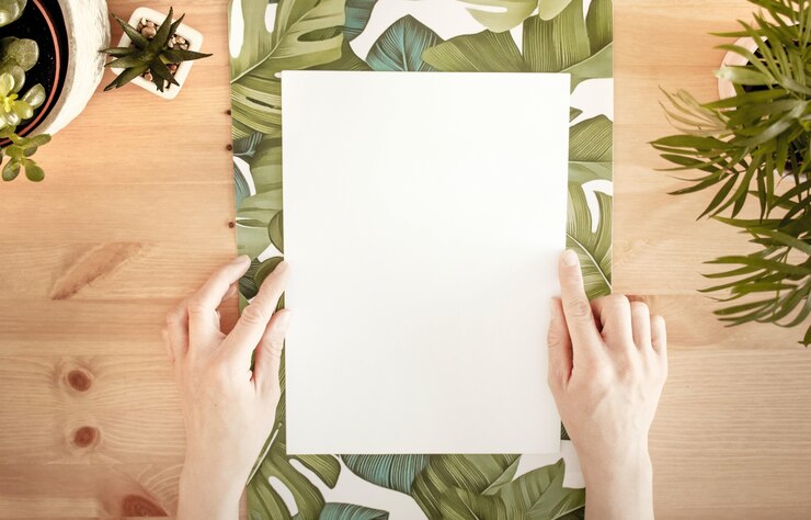 Foto grátis mãos tocando um papel branco com espaço para texto em uma superfície de madeira com plantas verdes