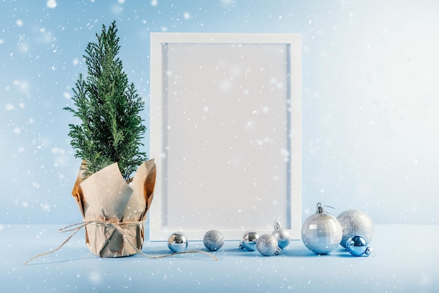 Maquete de natal com moldura branca, árvore de natal thuja e bolas de prata sobre fundo azul com neve caindo