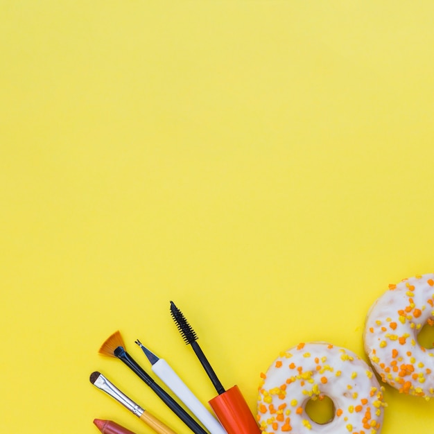 Maquiagem ferramentas e dois donuts em fundo amarelo