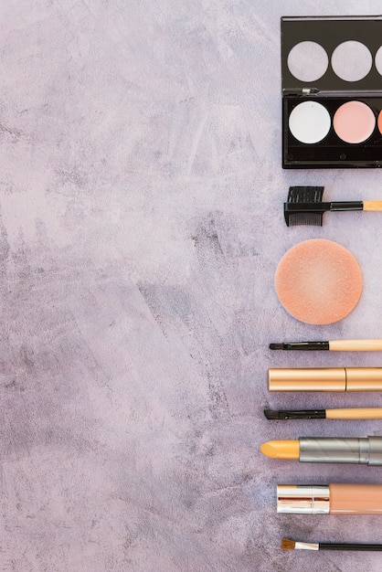 Foto grátis maquiagem paleta de sombra colorida com produtos cosméticos dispostos em uma fileira no fundo de concreto
