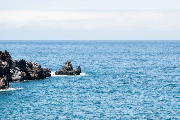 Mar azul lindo com pedras na costa