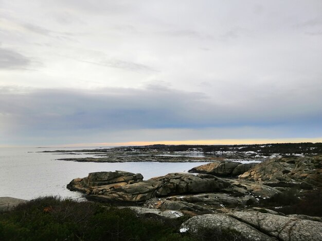 Mar cercado por rochas cobertas de galhos sob um céu nublado durante o pôr do sol na Noruega