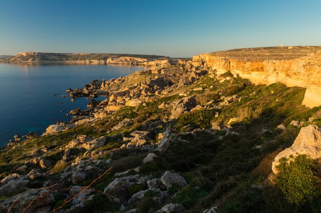 Mar cercado por rochas sob a luz do sol e um céu azul na costa noroeste, Malta