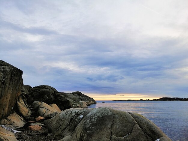 Mar cercado por rochas sob um céu nublado durante o pôr do sol em Stavern, na Noruega