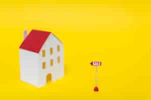 Foto grátis marca de venda na frente do modelo de casa borrão contra pano de fundo amarelo
