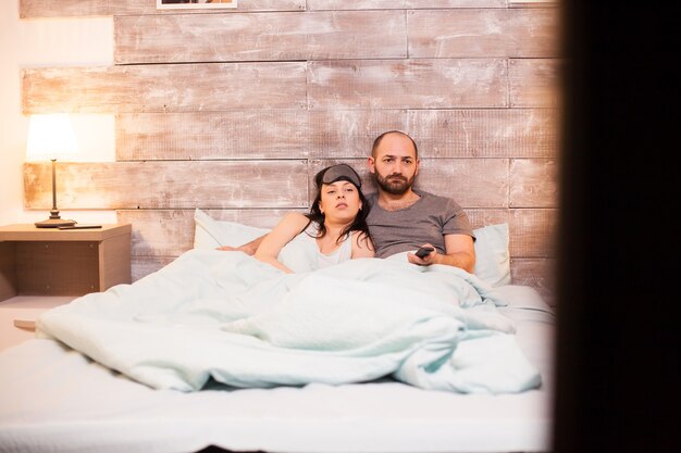 Marido e mulher caucasianos de pijama enquanto assistiam tv antes de dormir.