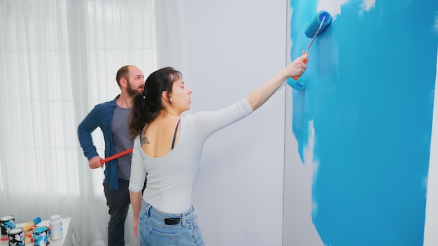 Marido e mulher pintando a parede durante a renovação da casa usando a escova de rolo. decoração de casa e reforma em apartamento aconchegante, reforma e reforma