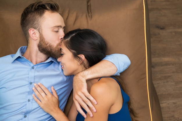 Marido feliz que beija sua esposa que encontra-se no sofá