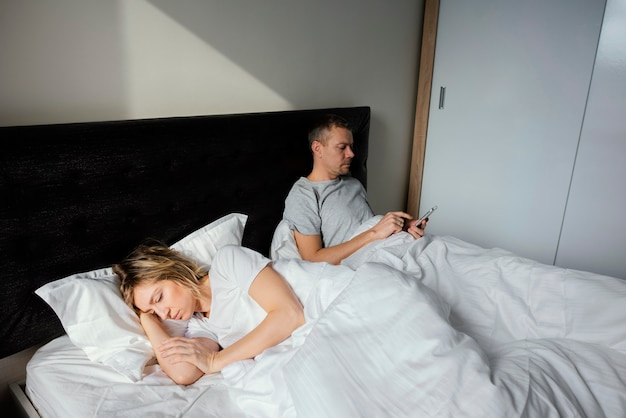 Marido usando celular enquanto a esposa está dormindo