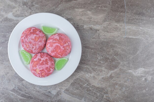 Marmeladas verdes e biscoitos rosa em uma travessa na superfície de mármore