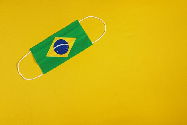 Máscara cirúrgica em fundo amarelo com bandeira do Brasil