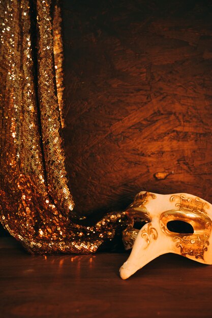 Máscara de disfarce branco com tecido de lantejoulas douradas de suspensão contra o plano de fundo texturizado