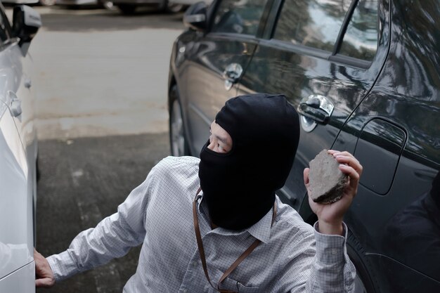 Mascarado ladrão usando uma balaclava segurando pedra pouco pronta para roubar carro