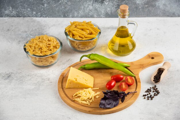 Massa crua, óleo, queijo e vegetais frescos em mármore.