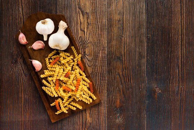 Massa de alho e fusilli na tábua sobre fundo texturizado de madeira