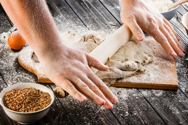 Massa de alongamento de Baker com um rolo e farinha sobre a tábua de cortar na mesa de madeira