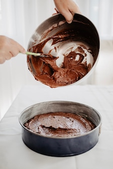 Massa de bolo de chocolate sendo transferida para uma forma redonda com espátula de silicone