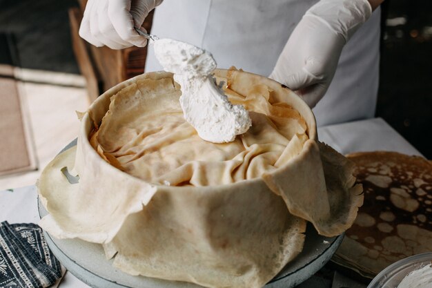 massa dentro de panela redonda com cozinheiro espalhando creme de leite nele dentro da cozinha